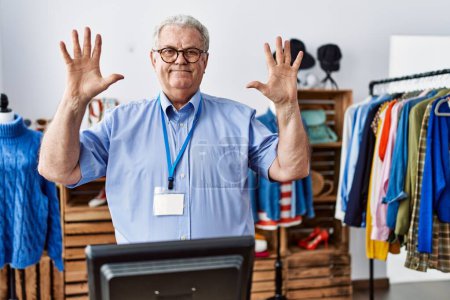 Foto de Hombre mayor con el pelo gris trabajando como gerente en boutique minorista mostrando y apuntando hacia arriba con los dedos número diez mientras sonríe confiado y feliz. - Imagen libre de derechos