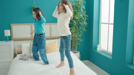 Téléchargez les photos : Deux enfants souriant danse confiante sur le lit dans la chambre - en image libre de droit
