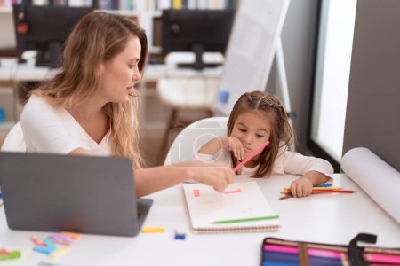 Téléchargez les photos : Enseignant et tout-petit assis sur la table dessinant sur ordinateur portable en classe - en image libre de droit