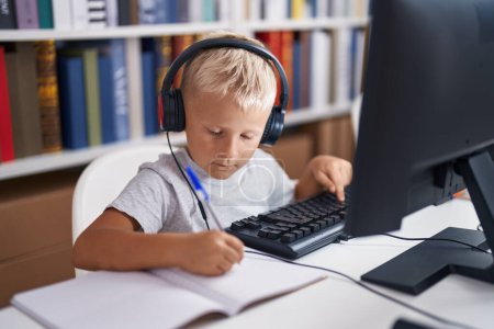 Photo for Adorable toddler student using computer writing on notebook at classroom - Royalty Free Image