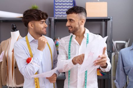 Téléchargez les photos : Two hispanic men tailors looking clothing design speaking at atelier - en image libre de droit