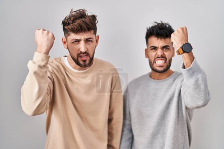 Téléchargez les photos : Young homosexual couple standing over white background angry and mad raising fist frustrated and furious while shouting with anger. rage and aggressive concept. - en image libre de droit