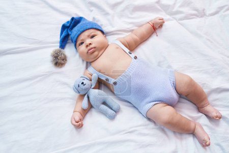 Photo for Adorable hispanic toddler wearing wool cap lying on bed at bedroom - Royalty Free Image
