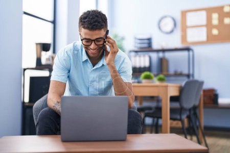 Foto de African american man business worker talking on the smartphone using laptop at office - Imagen libre de derechos