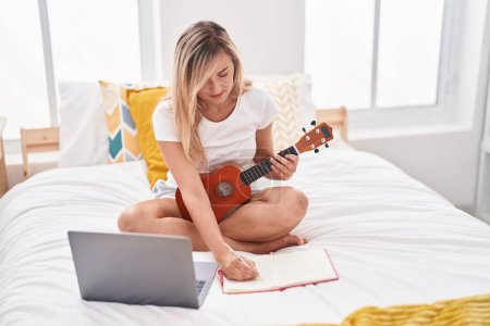 Téléchargez les photos : Jeune femme blonde ayant une leçon d'ukulélé en ligne composant la chanson dans la chambre - en image libre de droit