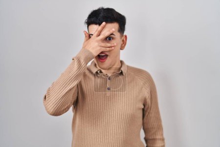 Photo for Non binary person standing over isolated background peeking in shock covering face and eyes with hand, looking through fingers with embarrassed expression. - Royalty Free Image
