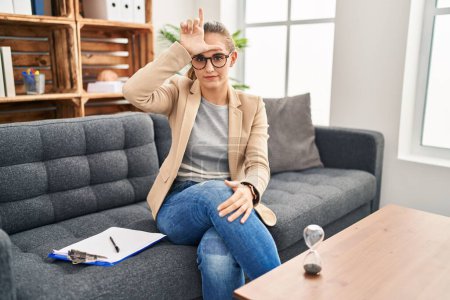 Photo for Young woman working at consultation office making fun of people with fingers on forehead doing loser gesture mocking and insulting. - Royalty Free Image
