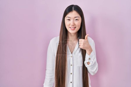 Téléchargez les photos : Chinese young woman standing over pink background doing happy thumbs up gesture with hand. approving expression looking at the camera showing success. - en image libre de droit