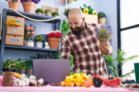 Photo for Young bald man florist using laptop holding plant at flower shop - Royalty Free Image