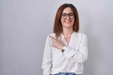 Foto de Brunette woman standing over white isolated background cheerful with a smile on face pointing with hand and finger up to the side with happy and natural expression - Imagen libre de derechos