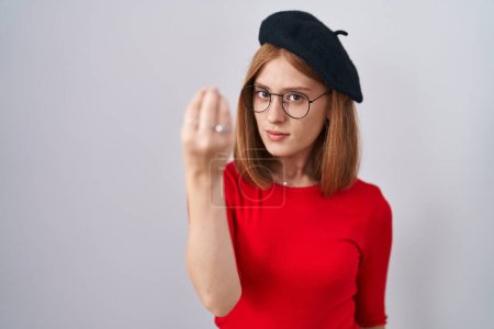 Foto de Young redhead woman standing wearing glasses and beret doing italian gesture with hand and fingers confident expression - Imagen libre de derechos