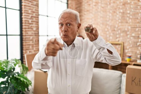 Téléchargez les photos : Senior man with grey hair holding virtual currency bitcoin pointing with finger to the camera and to you, confident gesture looking serious - en image libre de droit