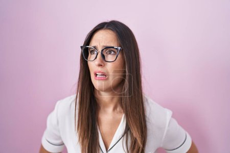 Téléchargez les photos : Young brunette woman wearing glasses standing over pink background with hand on stomach because indigestion, painful illness feeling unwell. ache concept. - en image libre de droit