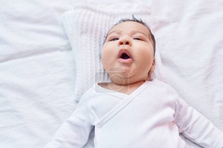 Téléchargez les photos : Adorable bambin hispanique souriant confiant couché sur le lit dans la chambre - en image libre de droit