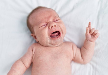Foto de Adorable caucasian baby lying on bed crying at bedroom - Imagen libre de derechos