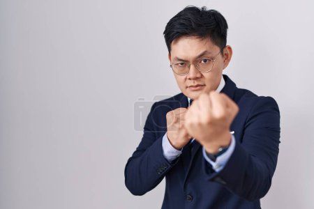 Photo for Young asian man wearing business suit and tie ready to fight with fist defense gesture, angry and upset face, afraid of problem - Royalty Free Image