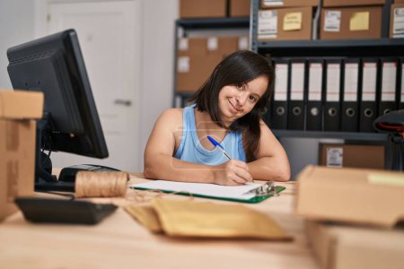 Téléchargez les photos : Femme trisomique ecommerce travailleur d'affaires écrivant sur la paperasserie au bureau - en image libre de droit