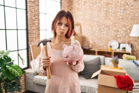 Téléchargez les photos : Young caucasian woman holding piggy bank at new home depressed and worry for distress, crying angry and afraid. sad expression. - en image libre de droit