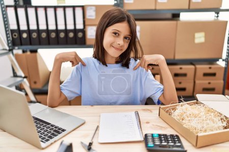 Young hispanic girl working at small business ecommerce looking confident with smile on face, pointing oneself with fingers proud and happy. 