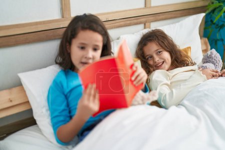 Téléchargez les photos : Two kids reading story book sitting on bed at bedroom - en image libre de droit