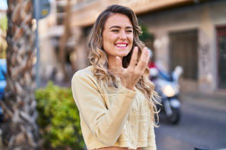 Téléchargez les photos : Young woman smiling confident doing coming gesture with finger at street - en image libre de droit