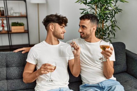 Téléchargez les photos : Two hispanic men couple toasting with glass of wine holding key of new house at home - en image libre de droit