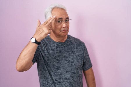 Foto de Middle age man with grey hair standing over pink background shooting and killing oneself pointing hand and fingers to head like gun, suicide gesture. - Imagen libre de derechos