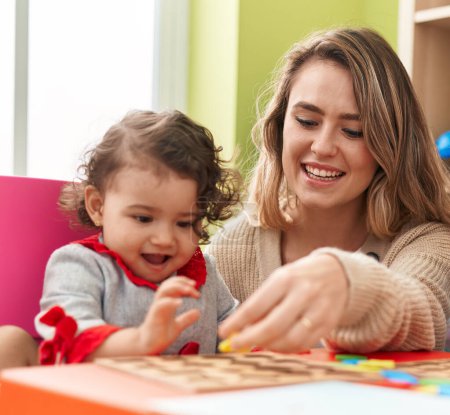Téléchargez les photos : Teacher and toddler playing with maths puzzle game sitting on table at kindergarten - en image libre de droit