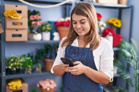 Photo for Young woman florist smiling confident using smartphone at florist - Royalty Free Image