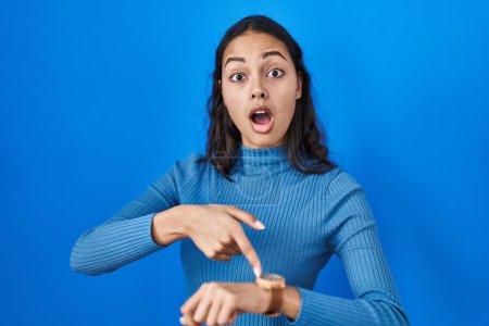 Téléchargez les photos : Young brazilian woman standing over blue isolated background in hurry pointing to watch time, impatience, upset and angry for deadline delay - en image libre de droit