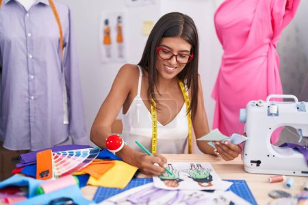 Téléchargez les photos : Jeune belle femme hispanique tailleur souriant conception de vêtements de dessin confiant au magasin de tailleur - en image libre de droit