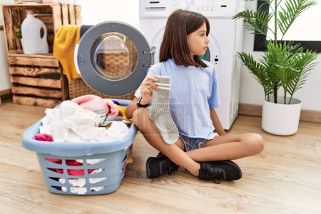 Téléchargez les photos : Young hispanic girl doing laundry holding socks looking to side, relax profile pose with natural face and confident smile. - en image libre de droit