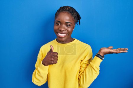 Photo for Beautiful black woman standing over blue background showing palm hand and doing ok gesture with thumbs up, smiling happy and cheerful - Royalty Free Image