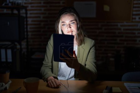 Photo for Blonde caucasian woman working at the office at night looking sleepy and tired, exhausted for fatigue and hangover, lazy eyes in the morning. - Royalty Free Image