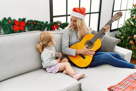 Foto de Madre e hija tocando la guitarra y cantando sentadas junto al árbol de Navidad en casa - Imagen libre de derechos