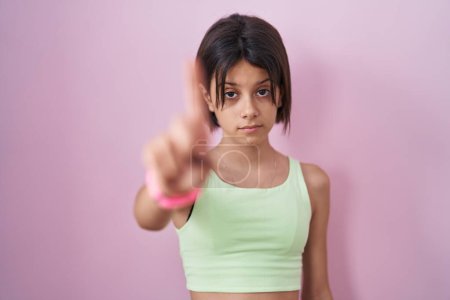 Foto de Young girl standing over pink background pointing with finger up and angry expression, showing no gesture - Imagen libre de derechos