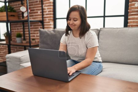 Téléchargez les photos : Femme trisomique utilisant un ordinateur portable assis sur le canapé à la maison - en image libre de droit