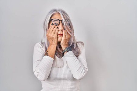 Téléchargez les photos : Middle age woman with grey hair standing over white background rubbing eyes for fatigue and headache, sleepy and tired expression. vision problem - en image libre de droit