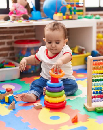 Téléchargez les photos : Adorable bébé hispanique jouant avec abaque et cerceaux jeu assis sur le sol à la maternelle - en image libre de droit