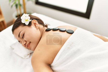 Photo for Young latin woman relaxed having back massage with black stones at beauty center - Royalty Free Image