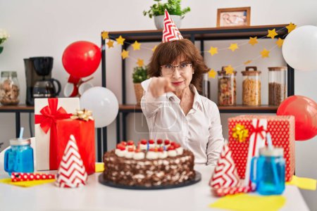 Photo for Middle age woman celebrating birthday holding big chocolate cake pointing with finger to the camera and to you, confident gesture looking serious - Royalty Free Image
