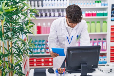 Photo for Young hispanic teenager pharmacist using touchpad and computer working at pharmacy - Royalty Free Image