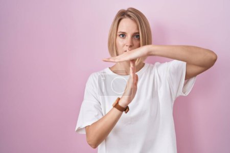 Foto de Joven mujer caucásica de pie sobre fondo rosa haciendo el gesto de tiempo fuera con las manos, rostro frustrado y grave - Imagen libre de derechos