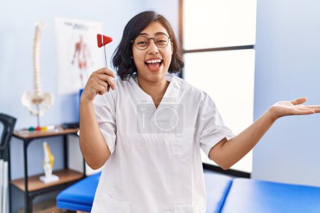 Foto de Young hispanic physiotherapist woman holding reflex hammer celebrating achievement with happy smile and winner expression with raised hand - Imagen libre de derechos