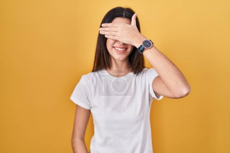 Photo for Young beautiful woman standing over yellow background smiling and laughing with hand on face covering eyes for surprise. blind concept. - Royalty Free Image