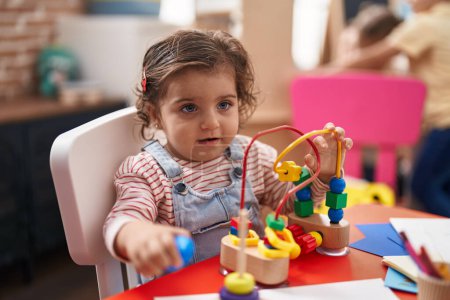 Foto de Adorable hispanic girl playing with toys sitting on table at kindergarten - Imagen libre de derechos