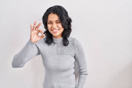Foto de Hispanic woman with dark hair standing over isolated background smiling positive doing ok sign with hand and fingers. successful expression. - Imagen libre de derechos