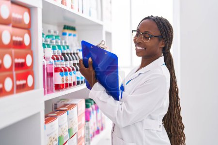 Téléchargez les photos : Une pharmacienne afro-américaine écrit sur un document à la pharmacie - en image libre de droit