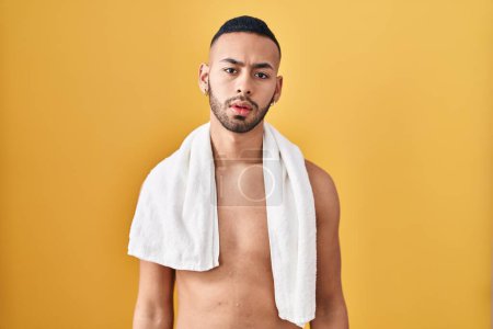 Téléchargez les photos : Jeune homme hispanique debout torse nu avec serviette à l'air endormi et fatigué, épuisé par la fatigue et la gueule de bois, les yeux paresseux le matin. - en image libre de droit