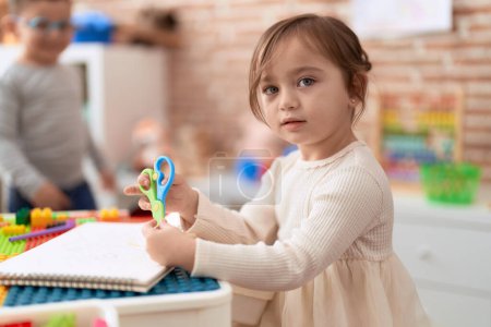 Téléchargez les photos : Adorable girl and boy sitting on table cutting paper at kindergarten - en image libre de droit